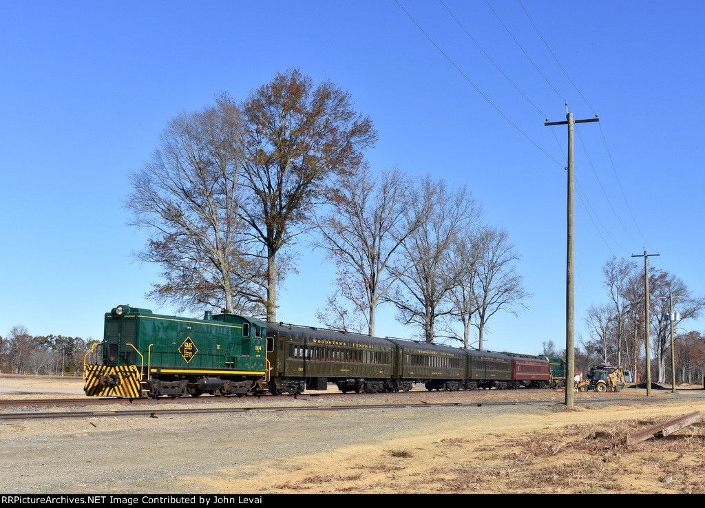 The diesel consist heads away from the photographers toward the S. Woodstown Station while a car on parallel Woodstown Alloway Rd outpaces the train. 